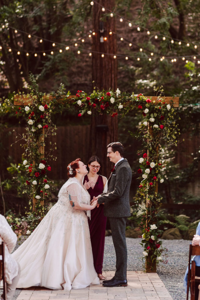 bride and groom holding hands under wooden ceremony arch with red & white flowers at Deer Park Villa