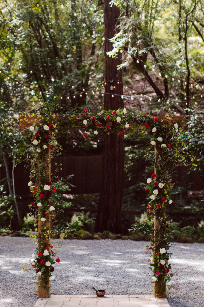wooden ceremony arch with white and red flowers and greenery at Deer Park Villa