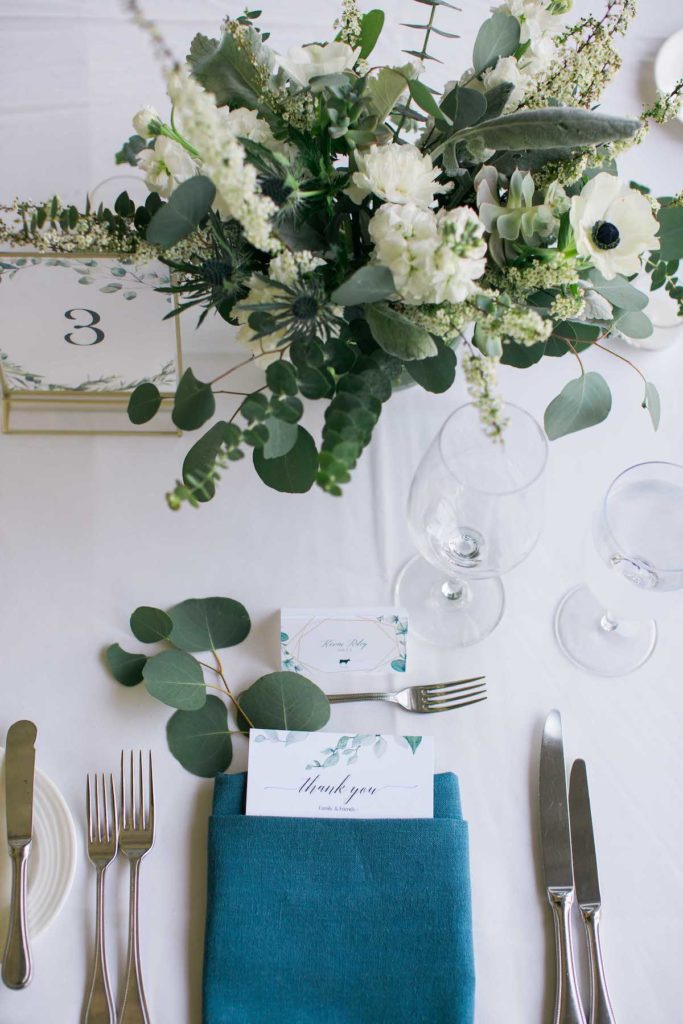 Reception table decor with blue napkin, silver silverware and green and white floral centerpiece