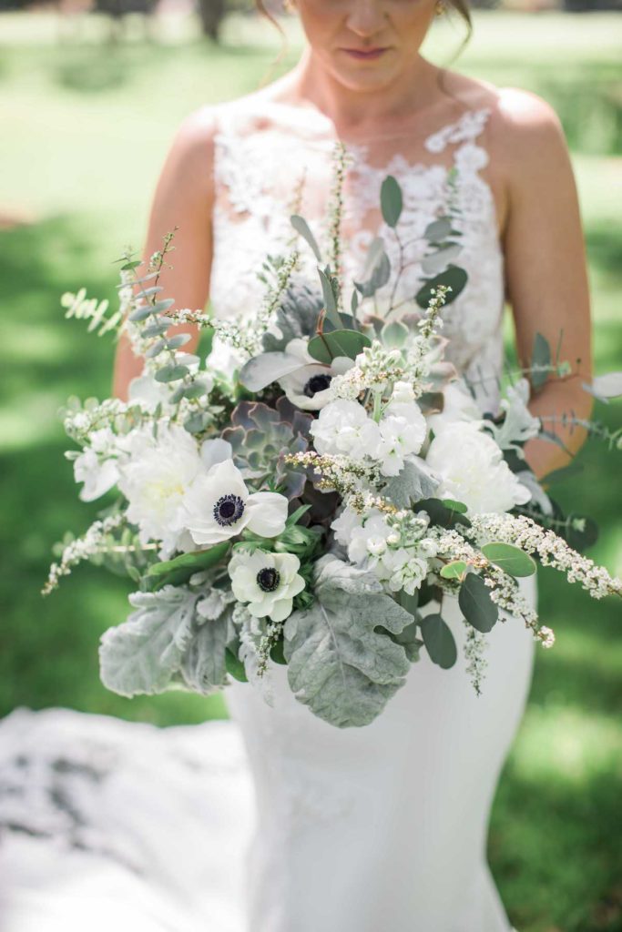 Bride holding white and green bridal bouquet and looking down at it