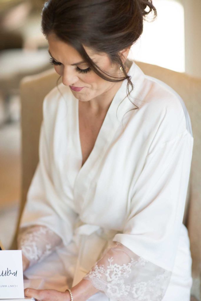 Bride writing the groom a handwritten note in white bridal robe