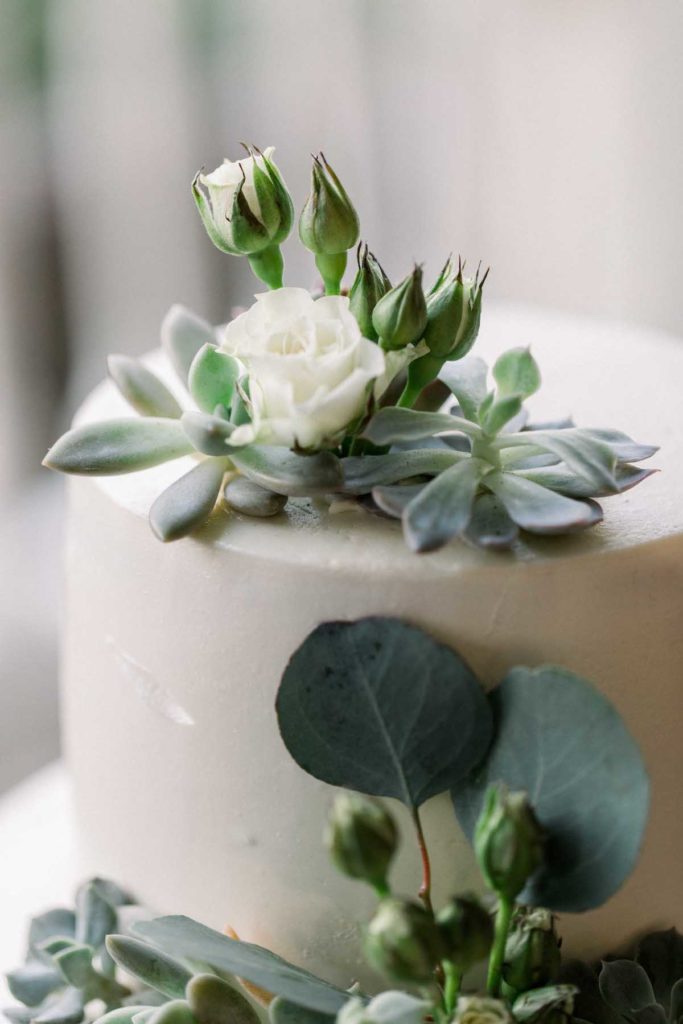 Close up of white wedding cake with succulents and white flowers