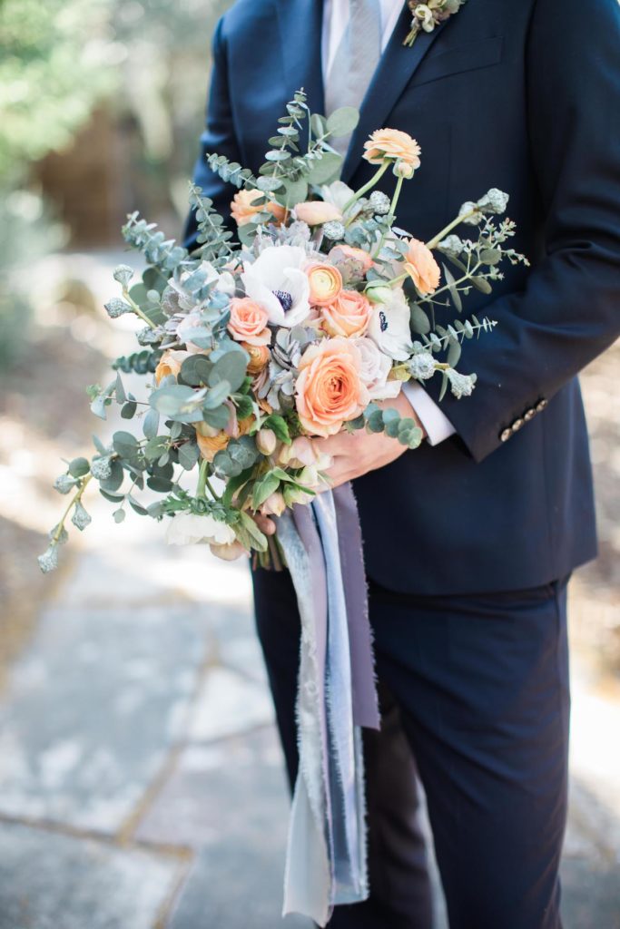 groom hold peach and white bridal bouquet with ranunculus and white anemones at Calistoga Ranch