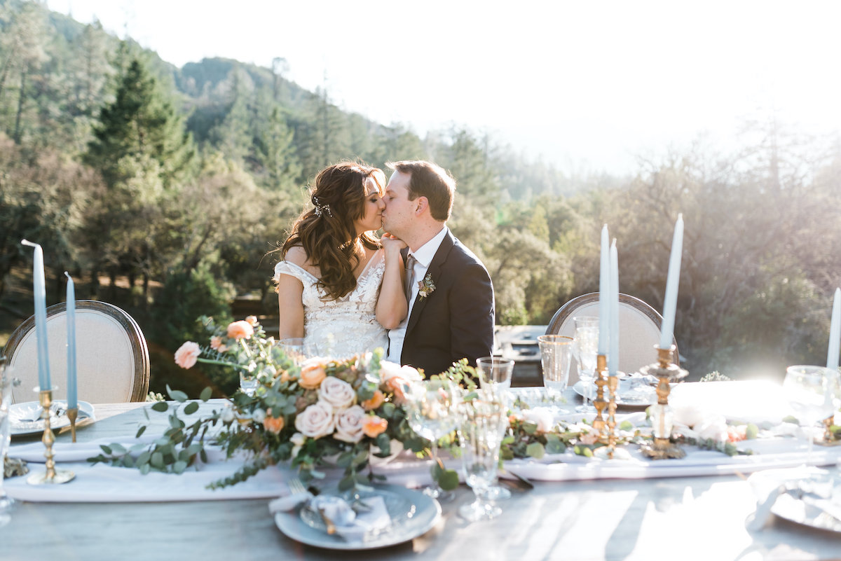 Bride and groom kissing while sitting at reception table